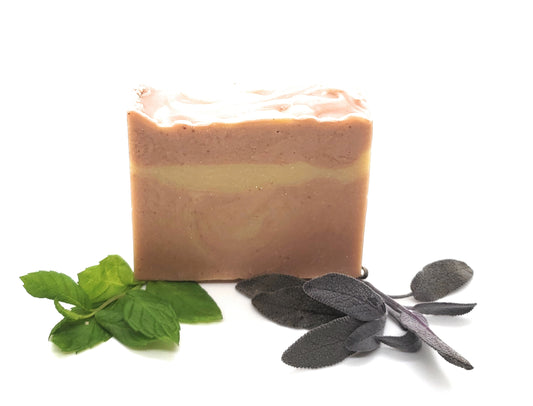 Pink ombre goat's milk soap on a white background with peppermint and sage fresh herbs. Patchouli, peppermint and clary sage goat's milk soap